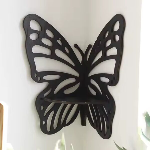 Black butterfly-shaped corner wall shelf mounted on a white wall, designed with cut-out wing patterns and a flat surface for placing small items.